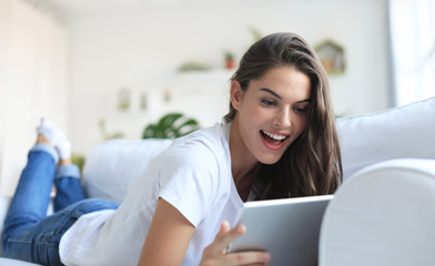 Beautiful young woman using tablet sitting on sofa at home at living room.