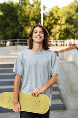 Photo of teenager boy 16-18 in casual wear standing with skateboard in skate park, during sunny summer day © Drobot Dean