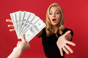 Woman looking at money which someone gives to her isolated over red background.