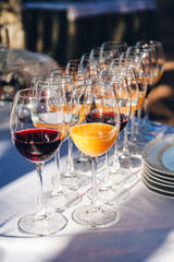 preparation for the holiday buffet - a lot of glasses with wine and juice on a white tablecloth in the rays of the sun close-up