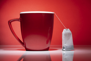Red mug and a tea bag on the red background