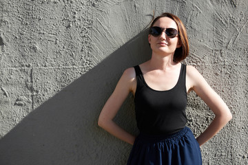 young girl posing against a concrete wall, dressed in black, hard light and shadows