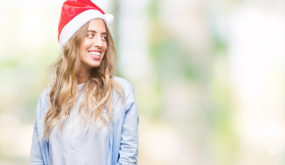 Beautiful young blonde woman wearing christmas hat over isolated background looking away to side with smile on face, natural expression. Laughing confident.