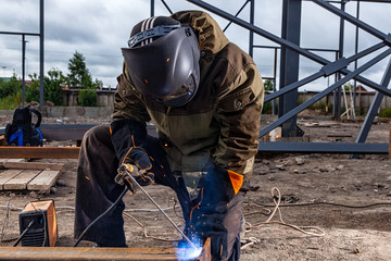 Close up welder weld metal pipe at construction site. A  builder in brown uniform, welding mask and...