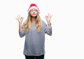 Fototapeta na wymiar Young beautiful blonde woman wearing christmas hat over isolated background relax and smiling with eyes closed doing meditation gesture with fingers. Yoga concept.