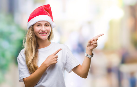 Young beautiful blonde woman wearing christmas hat over isolated background smiling and looking at the camera pointing with two hands and fingers to the side.