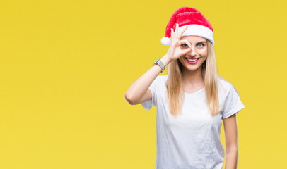 Young beautiful blonde woman christmas hat over isolated background doing ok gesture with hand smiling, eye looking through fingers with happy face.