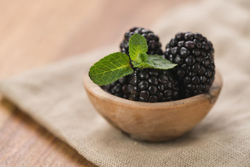 fresh blackberries in wood bowl on wooden table with mint leaves