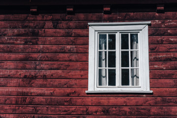 Fototapeta premium A white window on the wooden cottage of dark red and brown planks. Cabin window on the right side of a photograph, space for copy. Rustic and rural, traditional. Old school view.