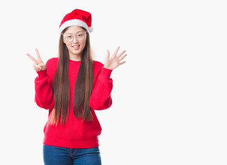 Young Chinese woman over isolated background wearing christmas hat showing and pointing up with fingers number seven while smiling confident and happy.