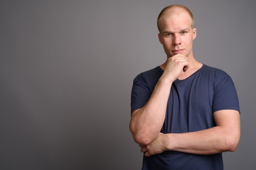 Bald man wearing blue shirt against gray background