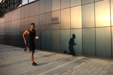 Full length of young African man in sports clothing jogging while exercising outdoors, at sunset or sunrise. Runner.
