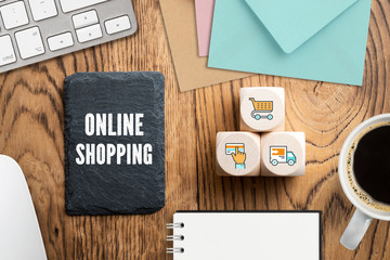 Schiefertafel mit Aufschrift "Online Shopping" und Würfel mit Einkauf-Symbolen am Computer-Arbeitsplatz