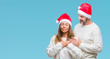 Middle age hispanic couple wearing christmas hat over isolated background smiling with hands on chest with closed eyes and grateful gesture on face. Health concept.