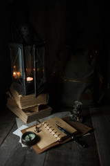 Old lamp and books lying on the table. A flame from an old source of light illuminating old prints. Black wooden background