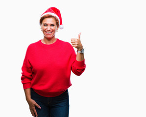 Atrractive senior caucasian redhead woman wearing christmas hat over isolated background doing happy thumbs up gesture with hand. Approving expression looking at the camera with showing success.
