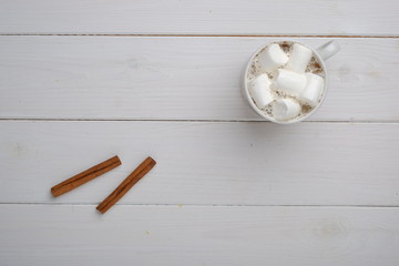 coffee cup with cinnamon, cinnamon sticks and marshmallow on white wood table top view with copy space for text 