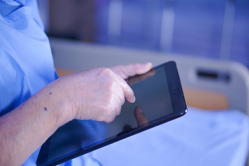 Asian senior or elderly old lady woman patient holding in her hands digital tablet and reading emails while sitting on bed in nursing hospital ward : healthy strong medical concept 
