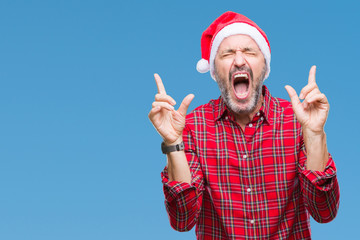 Naklejka premium Middle age hoary senior man wearing christmas hat over isolated background celebrating mad and crazy for success with arms raised and closed eyes screaming excited. Winner concept