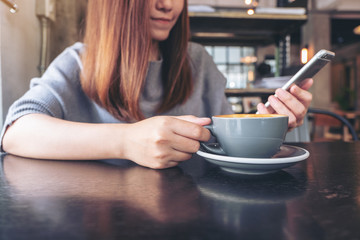 Closeup image of a woman holding and using a smart phone while drinking coffee