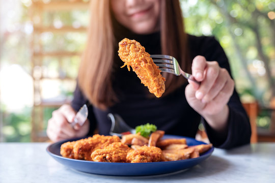 Closeup image of a beautiful asian woman using knife and fork to eat fried chicken and french fries in restaurant