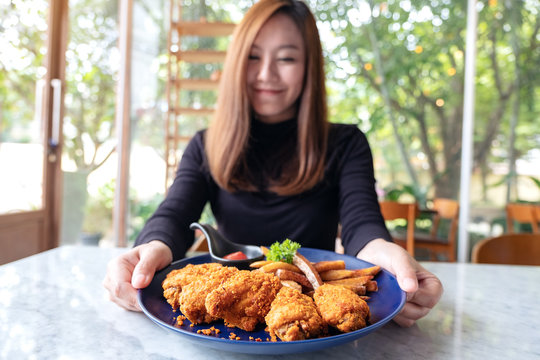 Closeup image of a beautiful asian woman holding and showing a plate of fried chicken and french fries in restaurant