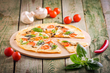 Close up slices of homemade pizza with mozzarella cheese, tomato, mushrooms and basil on wood table with ingredients