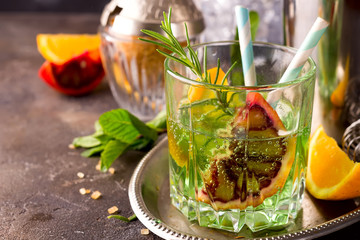 Sweet refreshing mint liqueur, with ice, red mandarin and rosemary on the metal tray to feed on gray concrete stone table,