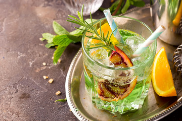 Sweet refreshing mint liqueur, with ice, red mandarin and rosemary on the metal tray to feed on gray concrete stone table,