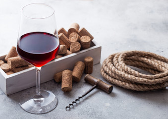 Elegant glass of red wine with box of corks and opener on stone kitchen table background.