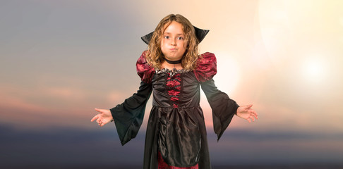 Fototapeta premium Kid dressed as a vampire at halloween holidays makes funny and crazy face emotion at outdoor with sunset