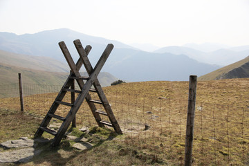 Fototapeta premium Stile over a fence in the misty and hazy mountains of Snowdonia with Snowdon shown in the background