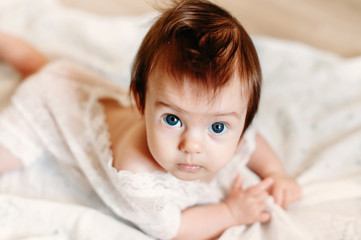 Cute and beautiful caucasian three months baby girl wearing in a white lace infant clothes and looking into the camera.