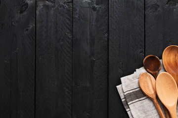 Wooden spoons and dishtowel on black wooden background with copy space. Top view of various types...