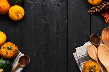 Autumn vegetables cooking preparation. Top view of pumpkins, wooden spoons and dishtowel on black...