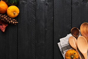 Autumn vegetables cooking preparation. Top view of pumpkins, wooden spoons and dishtowel on black wooden background with copy space.