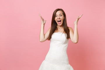 Portrait of pretty amazed surprised bride woman in exquisite white wedding dress standing spreading hands isolated on pink pastel background. Wedding celebration concept. Copy space for advertisement.