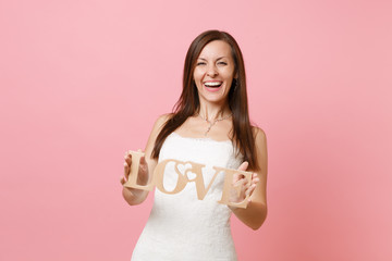 Portrait of laughing happy bride woman in lace white wedding dress standing and holding wooden word...