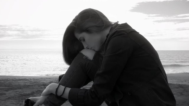 Woman feeling alone and sad at dawn in front of the ocean in winter black and white medium shot
