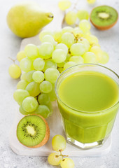 Glass of fresh smoothie organic green toned fruit on white chopping board on stone kitchen background. Pear and grapes with kiwi and lime and apple.