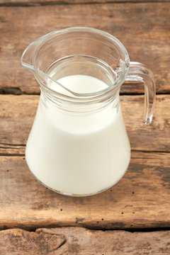 Transparent jug with milk on wooden background. Fresh organic milk in glass jug on rustic wooden boards.