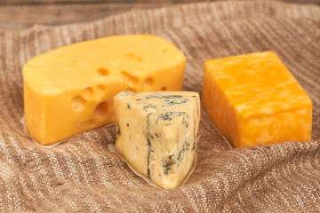 Different type of cheese on wooden background. Dutch cheese, French gorgonzola cheese and marble cheese on sackcloth. Food for dairy gourmet.