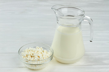 Dairy products background. Cottage cheese and glass jug of fresh milk on light wooden background.