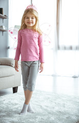 Obraz premium I am little fairy. Full length portrait of elegant girl wearing pink wings and crown. She is standing in house and smiling 