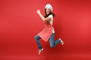 Housewife female chef cook or baker in striped apron white t-shirt, toque chefs hat isolated on red wall background. Full length portrait housekeeper woman jumping high up. Mock up copy space concept. - Powered by Adobe