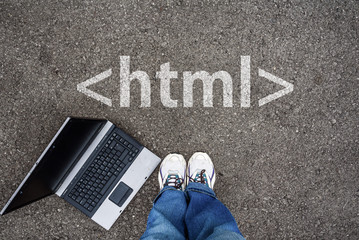  man legs in sneakers standing next to laptop and html tag on asphalt