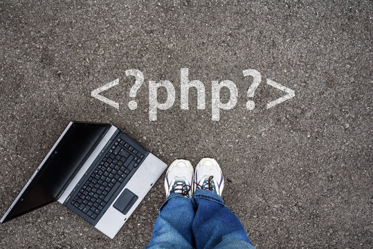 man legs in sneakers standing next to laptop and php tag on asphalt