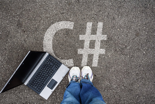  man legs in sneakers standing next to laptop and c sharp, c#  on asphalt