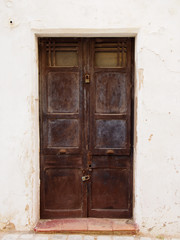 old wooden brown double doors with chipped flaking faded peeling paint and rusty handles padlocked closed in a white painted wall and tile doorstep