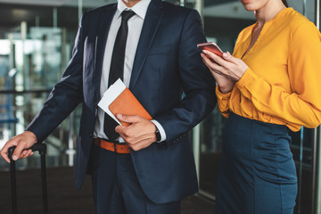 Businessman holding passport with tickets. His female assistant typing on handy